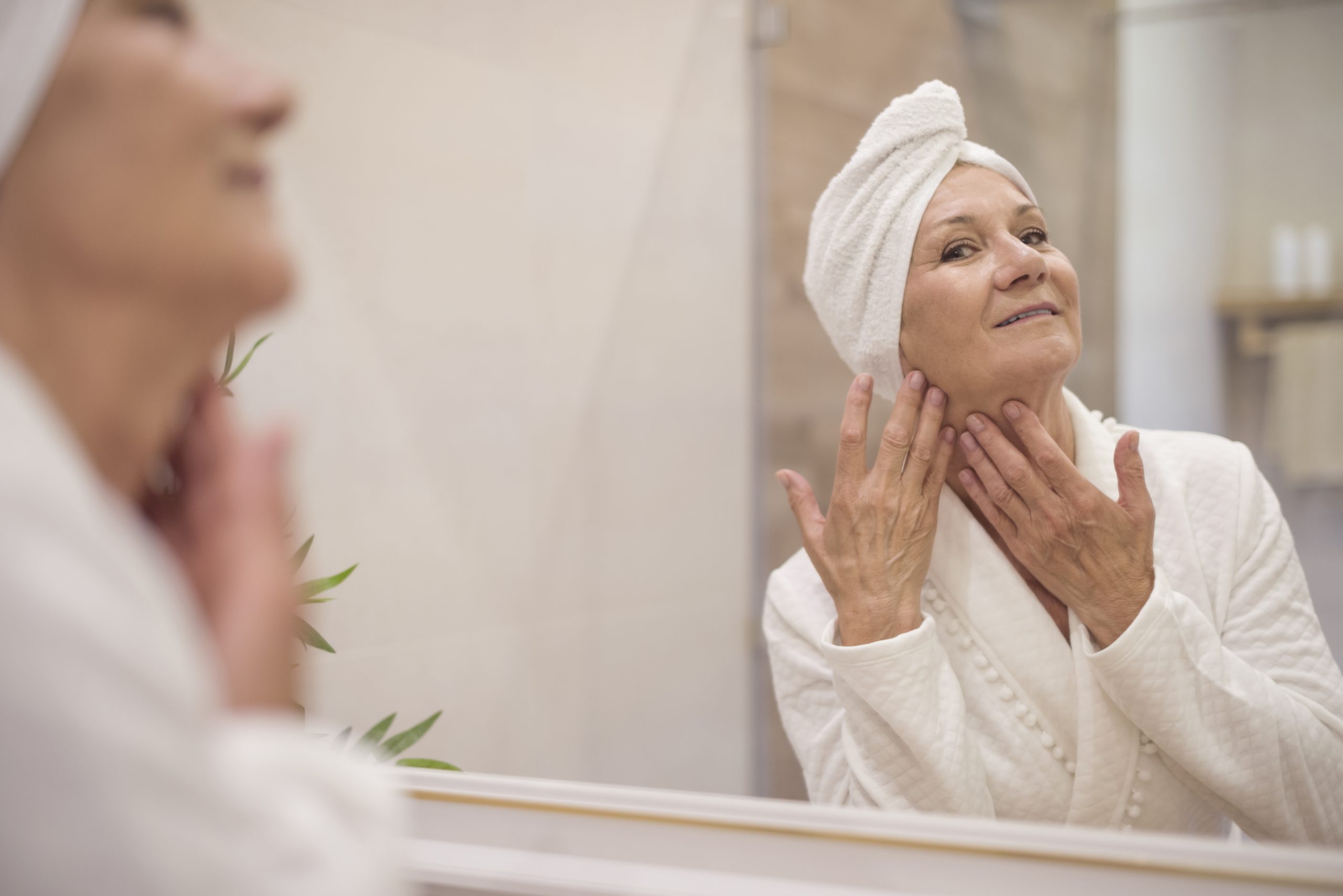 mulher mais velha em um pós banho tocando a pele e se olhando no espelho