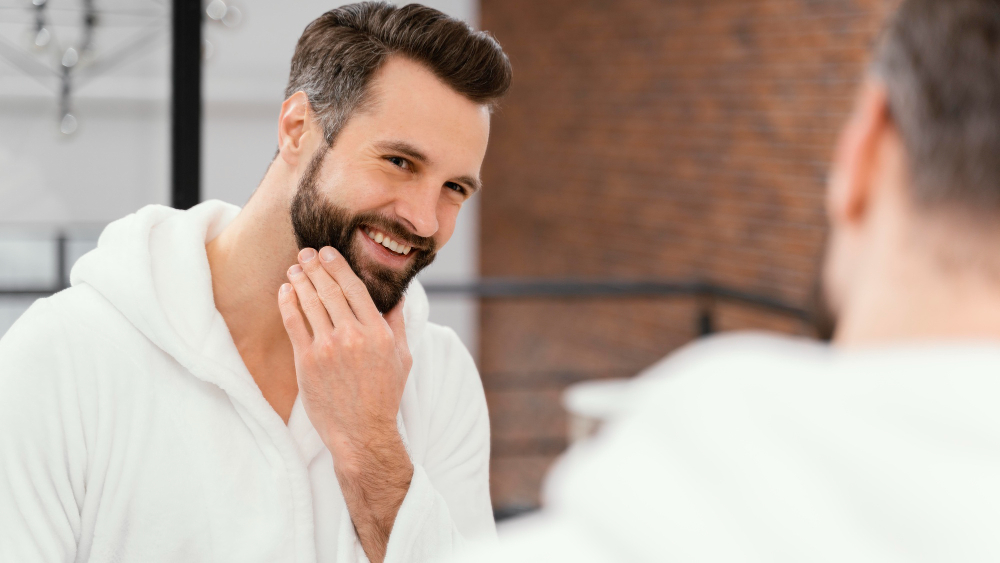 homem branco em frente ao espelho se olhando passando a mão na barba