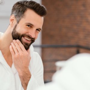 homem branco em frente ao espelho se olhando passando a mão na barba
